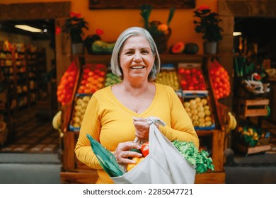 Zero waste food retail - Happy senior woman holding reusable bag of fresh vegetables at local market store - Sustainable eco concept - Focus on face - Powered by Shutterstock