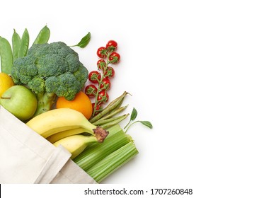 Zero waste food shopping with reusable bags. Flat lay with fruits and vegetables in textile tote bag isolated on white background with copyspace.