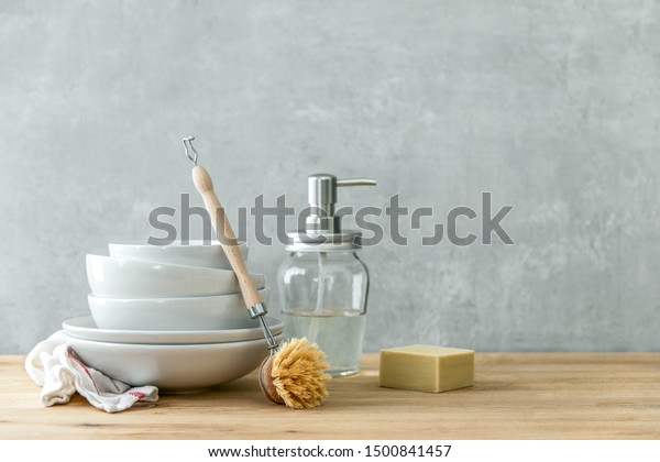 Zero waste home kitchen cleaning concept, front view\
of dishes, dish washing brush and eco safe soap, blank space for a\
text