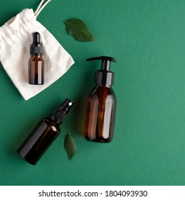 Zero Waste Organic SPA Cosmetics Set With Green Leaves. Top View Amber Glass Bottles On Green Background. Natural Skincare Beauty Products Packaging Design.