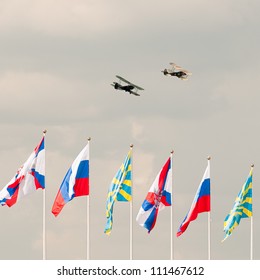 ZHUKOVSKY, MOSCOW REGION/RUSSIA - AUGUST 10: Polikarpov Po-2 (U-2, Kukuruznik) Mule General-purpose Soviet Biplanes Above Flags Of Russia, Ministry Of Defense And DOSAAF On Cloudy Sky Background.