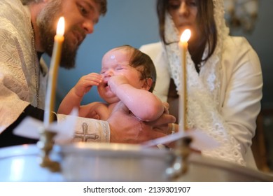 Zhytomyr, Ukraine - September 12, 2021: Newborn baby baptism in Holy water. Infant bathe in water. Baptism in the font. Sacrament of baptism. Child and God. Christening candle Holy water font.