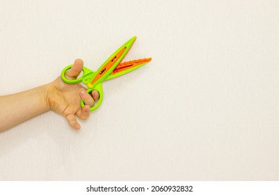 Zigzag Scissors For Cutting Paper On Blue,orange Or Wooden Floor Surface.man Or Kid Hand Is Holding Scissors Against The Wall.activities For Children's Concept,education,development,back To School.