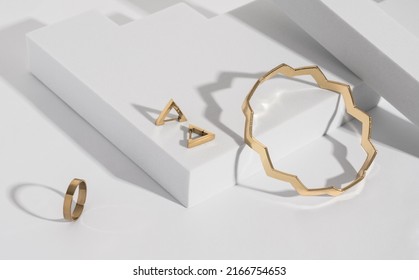 Zigzag Shape Golden Bracelet And Modern Earrings And Ring On Geometric White Background