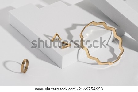 Zigzag shape golden bracelet and modern earrings and ring on geometric white background