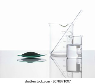 Zinc Powder In Chemical Watch Glass Place Next To Crystal Clear Liquid In Beaker. Closeup Chemical Ingredient On White Laboratory Table. Side View