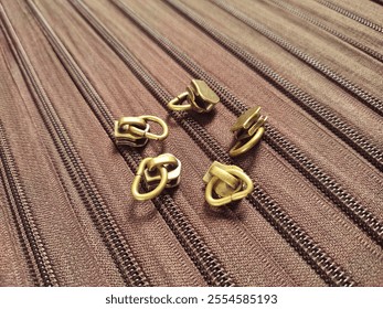 The zipper slider sits atop a stack of striped brown zippers that also serve as a background
