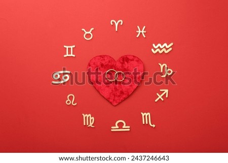 Zodiac signs, heart and wedding rings on red background, flat lay