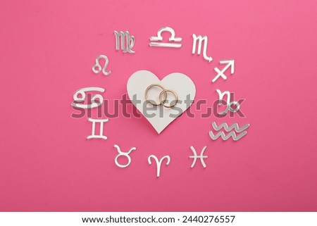Zodiac signs, heart and wedding rings on pink background, flat lay