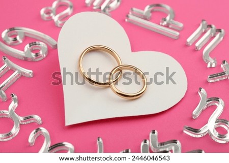 Zodiac signs, heart and wedding rings on pink background, closeup