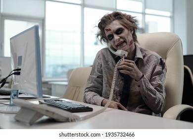 Empresario zombiano con receptor de teléfono entre el hombro y la mejilla mirando la pantalla del ordenador