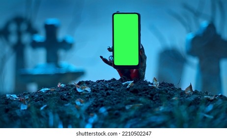 Zombie hand rising up smartphone with green screen out of grave. Holiday event halloween concept. - Shutterstock ID 2210502247