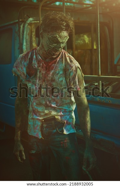 Zombie man. A scary bloodied zombie stands by an old car\
in a ruined city on a sunset. Zombie apocalypse. Halloween. Horror\
movie. 