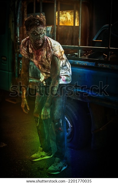Zombie man. A scary bloodied zombie stands leaning on an\
old car in a ruined city. Zombie apocalypse. Halloween. Horror\
movie. 