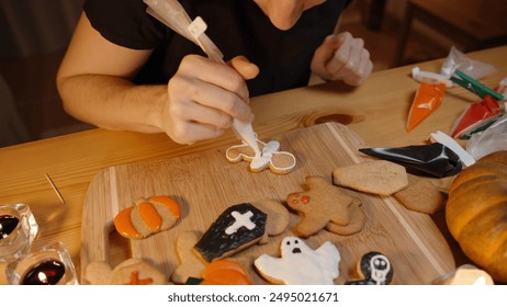 Zoom In, a Woman Uses White Icing to Add Details to One of the Man-Shaped Cookies. The Cookies Have Various Forms and Decorations Related to Halloween, Including Pumpkins, Ghosts, and Crosses. - Powered by Shutterstock