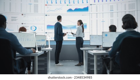 Zoom Out Back View Shot Of Male And Female Analysts Discussing Financial Data On Big Digital Screen In Monitoring Office. Diverse Employees Working Behind Desktop Computers In Venture Capital Company. - Shutterstock ID 2348534985