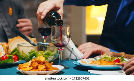 Zoom In Shot Of Young Man Pouring Red Wine Into A Glass At Family Dinner.