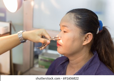 Zooming closeup portrait lateral view a middle-aged Asian woman has been examining by a doctor who inserting a nasal speculum to widen her left nostril to find out something wrong inside - Shutterstock ID 691606822
