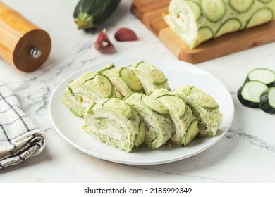 Zucchini roll stuffed with cream cheese, garlic and tomatoes. Green squash roll slices on the white plate on the white marble background - Powered by Shutterstock