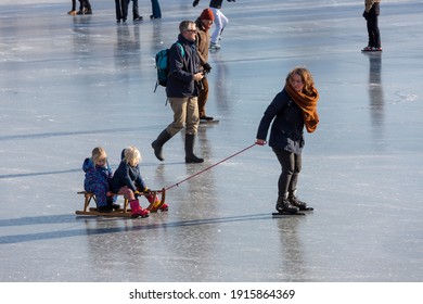 Zutphen, The Netherlands - February 12, 2021: Mother On Ice Skates Dragging A Rope With A Sledge And Two Children On Open Water Canal