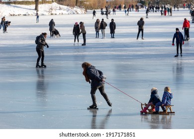 Zutphen, The Netherlands - February 12, 2021: Cozy Scenery With Mother Towing Children On A Sledge On Urban Frozen Open Water Canal With Other Recreants In The Background