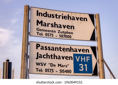 Zutphen, The Netherlands - March 31, 2021: Weather Data Collection Mast And Marine Traffic Directions Sign Pointing To Industrial And Recreational Harbor Against A Sunset Sky With Clouds