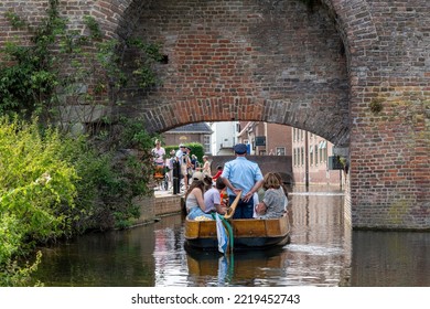 Zutphen, The Netherlands-August 2022; Close Up Of A Small Cruise Boat With Captain Standing Going Under The Medieval Berkel Poort Or Water Gate And Fortified Wall Of The City With Tourists On Board