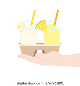 The 2 glasses of juice smooties (pineapple, banana). They are in the cup carier that hold in hand. take a way beverages. home delivery concept. organic and healthy soft drink for summer.