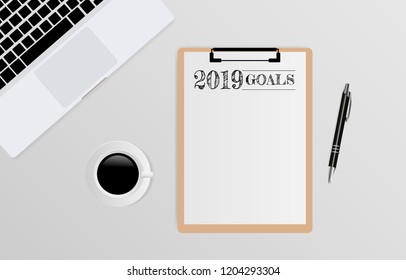 2019 Goals text on white paper on clipboard with laptop, pen and coffee cup on gray background