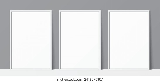 3 blank white poster frames leaning against a grey wall background. Poster gallery vector mockup for art, image, or text placement.