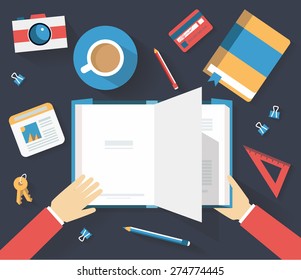 Above look on the office table with man reading the book, notebook, keys, ruler, photo camera, credit card, photo, cup of coffee, pencils and binders