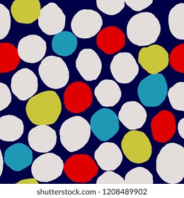 Abstract seamless pattern with irregular dots in blue, yellow, cream and red on dark blue background.