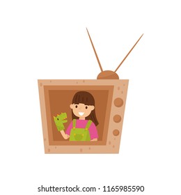 Adorable smiling girl sitting in TV made of cardboard box and playing with toy dragon on hand. Flat vector design