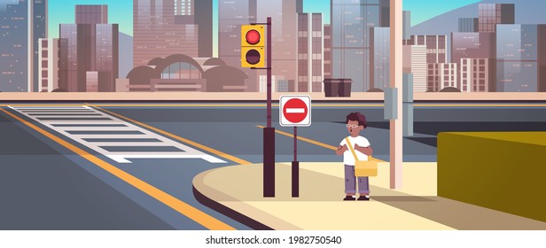 african american schoolboy with backpack standing on city street near red stop road sign road safety concept cityscape