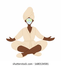 African american woman in bathrobe, towel and face mask meditating in lotus pose. Home spa relaxing with cucmber slices on eyes.