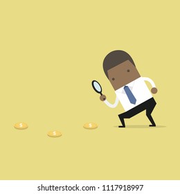African businessman holding a magnifying glass follow dollar coins.