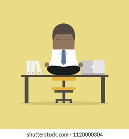 African businessman meditation in office. yoga at job. young man relaxing in lotus position on table with computer at work.