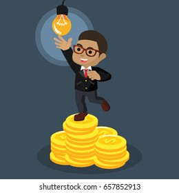 african businessman on stack of coin trying to reach bulb