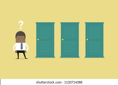 African businessman standing beside three doors, unable to make the right decision concept with question marks above his head.