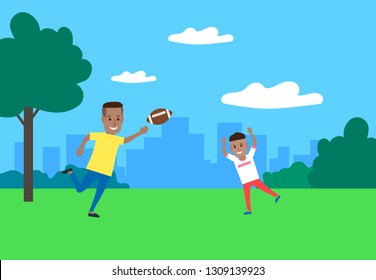 african father and son playing american football together in the park