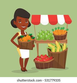 An african greengrocer standing near stall with fruits and vegetables. Greengrocer standing near market stall. Greengrocer holding basket with fruits. Vector flat design illustration. Square layout.