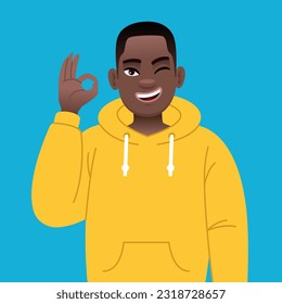 African successful confident boy in yellow hoodie shows ok sign gesture. Happy black young guy with glasses. Vector illustration in cartoon style on a blue background.