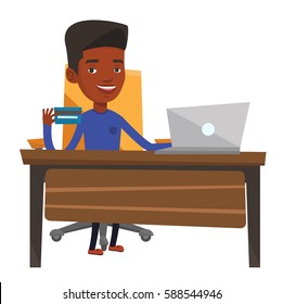 African Young Man Sitting At The Table With Laptop And Credit Card In Hand. Man Using Laptop For Online Shopping. Man Showing Credit Card. Vector Flat Design Illustration Isolated On White Background.