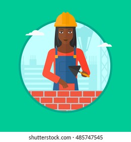 African-american bricklayer in uniform and hard hat. Bricklayer working with a spatula and a brick in hands on construction site. Vector flat design illustration in the circle isolated on background.