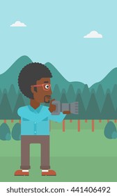 An african-american man taking photo on the background of green forest and mountains vector flat design illustration. Vertical layout.