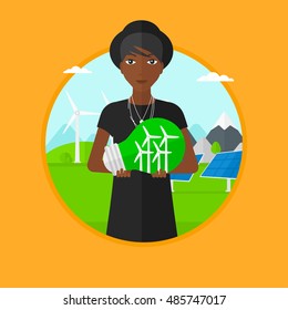 An african-american woman holding light bulb with small wind turbines inside on a background with solar pannels and wind turbines. Vector flat design illustration in the circle isolated on background.