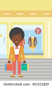 African-american woman holding shopping bags on the background of boutique window with dressed mannequins. Happy young woman carrying shopping bags. Vector flat design illustration. Vertical layout.