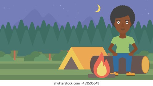 An african-american woman sitting on a log near a fire on a background of camping site with tent. Woman sitting near a campfire at a campsite. Vector flat design illustration. Horizontal layout.