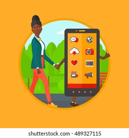An african-american woman walking with a big smartphone. Woman and a big smartphone in the park. Woman holding hand of smartphone. Vector flat design illustration in the circle isolated on background