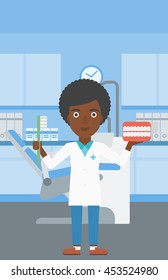 An african-american young female dentist holding dental jaw model and a toothbrush in doctor office. Vector flat design illustration. Vertical layout.